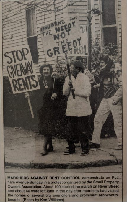 One marcher holds a sign Stop Giveaway Rents. Another, Peggy Wolynes, holds a sign Housing For the Needy Not the Greedy. Two more stand behind them.